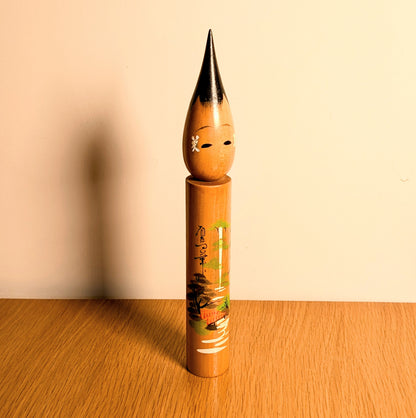 Poupée japonaise kokeshi pinceau en bois, présentée en ambiance intérieure chaude, souvenir d’Arima Onsen