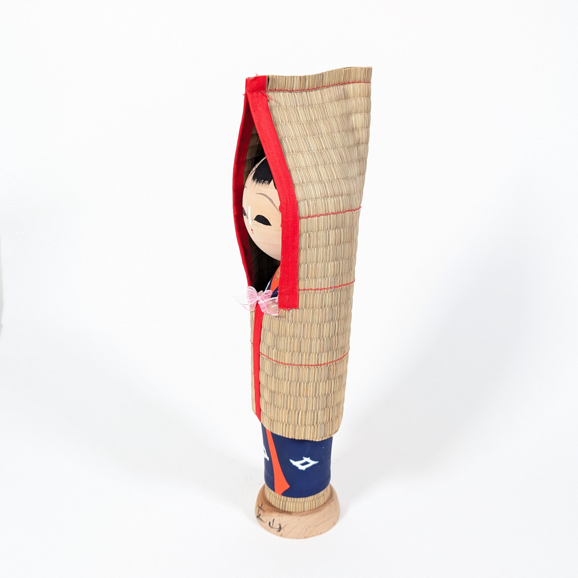 Kokeshi japonaise de profil avec manteau de paille mino, objet mingei d’art populaire japonais inspiré des régions enneigées