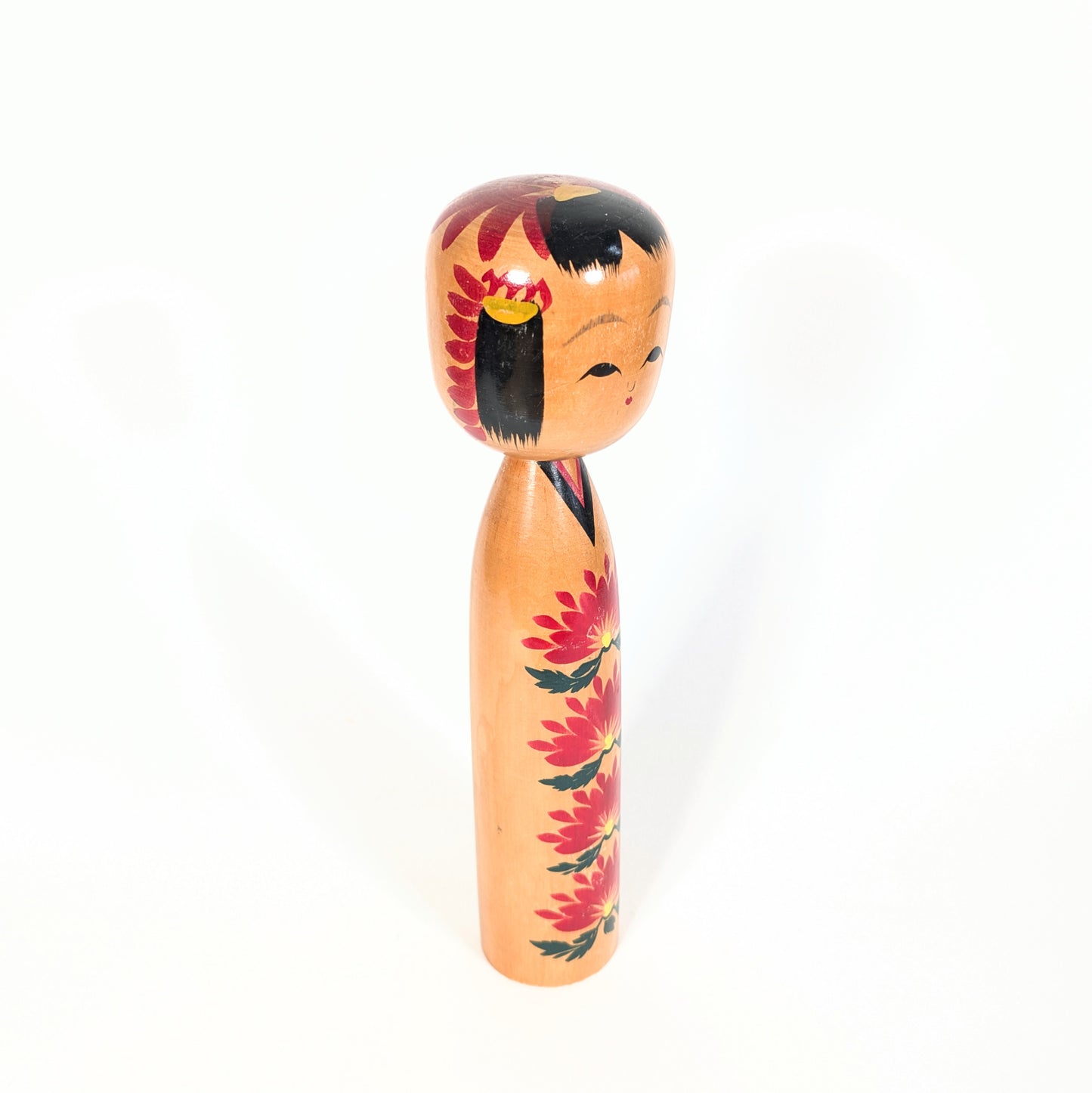 Vue de profil d’une kokeshi Ryosaku 良作 avec motifs kiku rouges, coiffure noire traditionnelle et style shingata élégant.