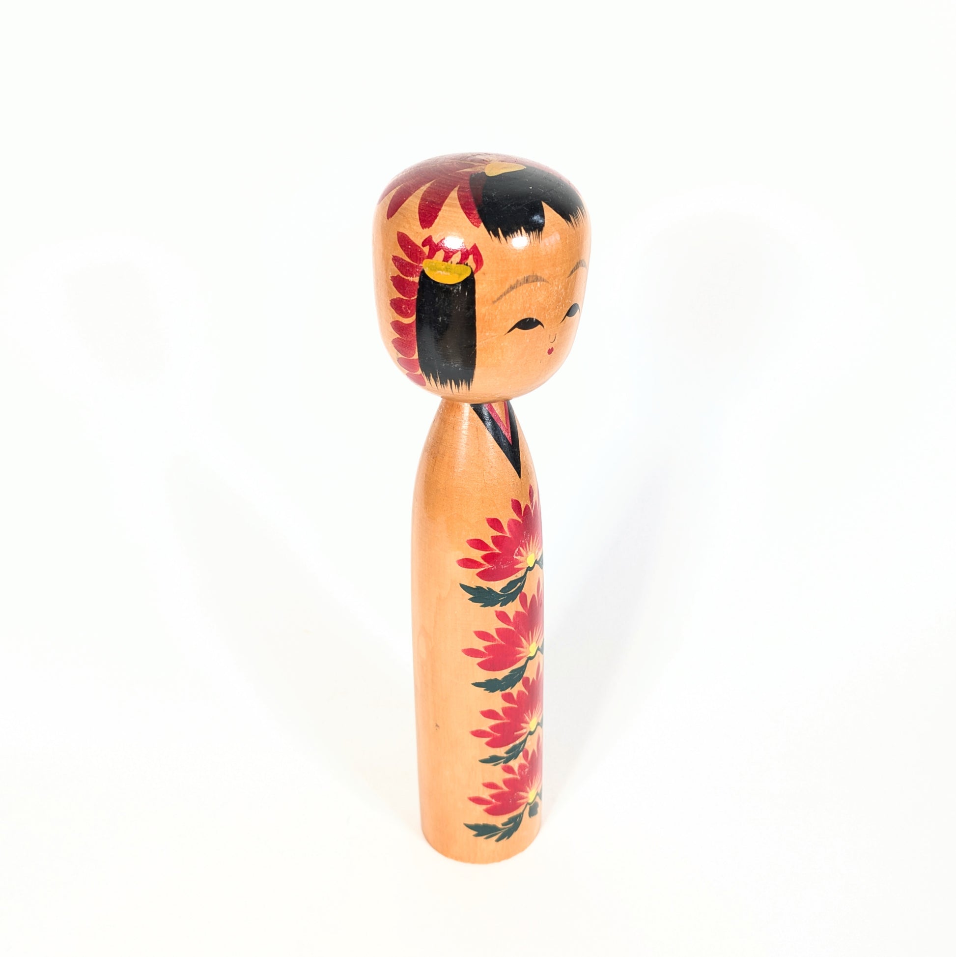 Vue de profil d’une kokeshi Ryosaku 良作 avec motifs kiku rouges, coiffure noire traditionnelle et style shingata élégant.