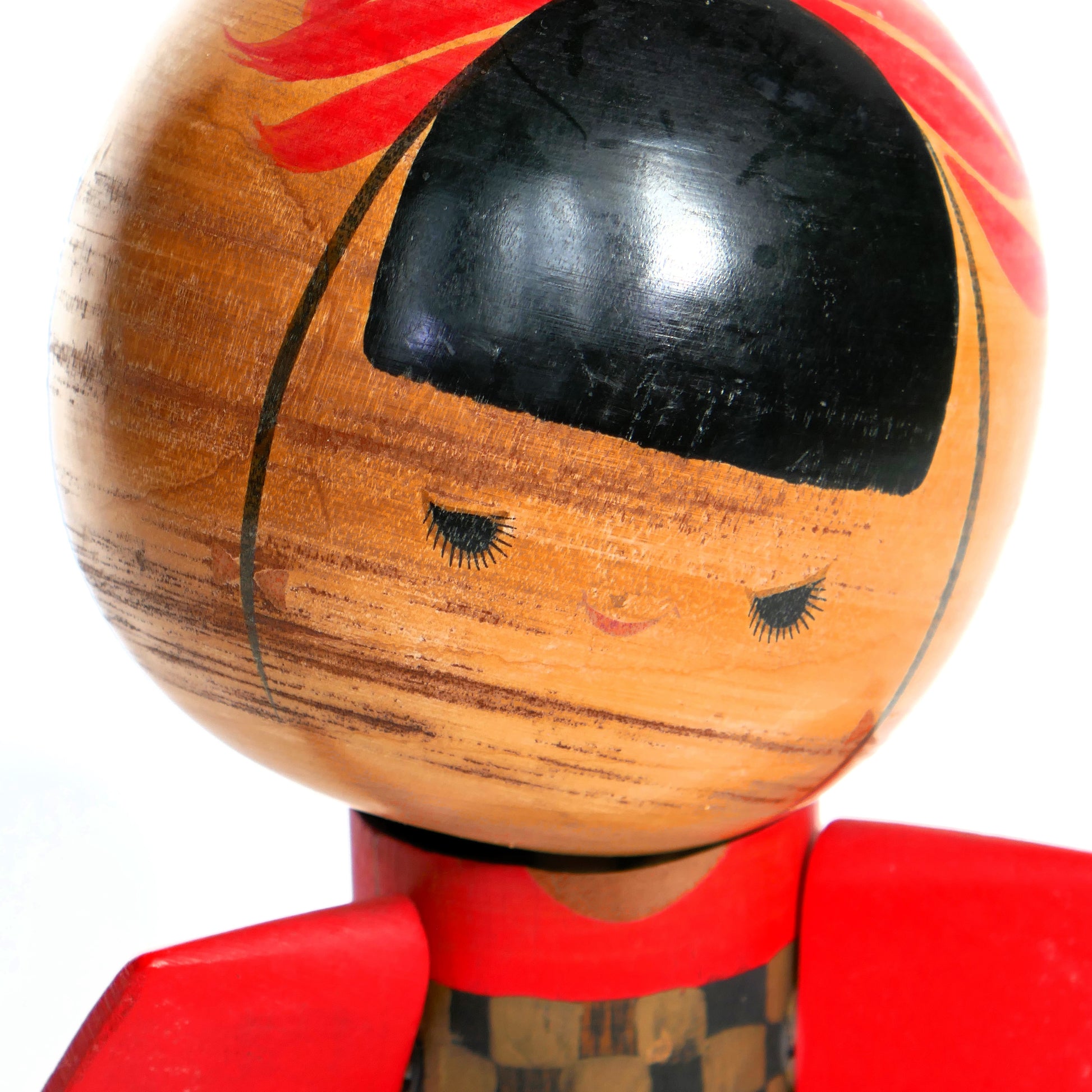 Gros plan sur le visage peint de la kokeshi vintage, coiffure noire et ruban rouge.