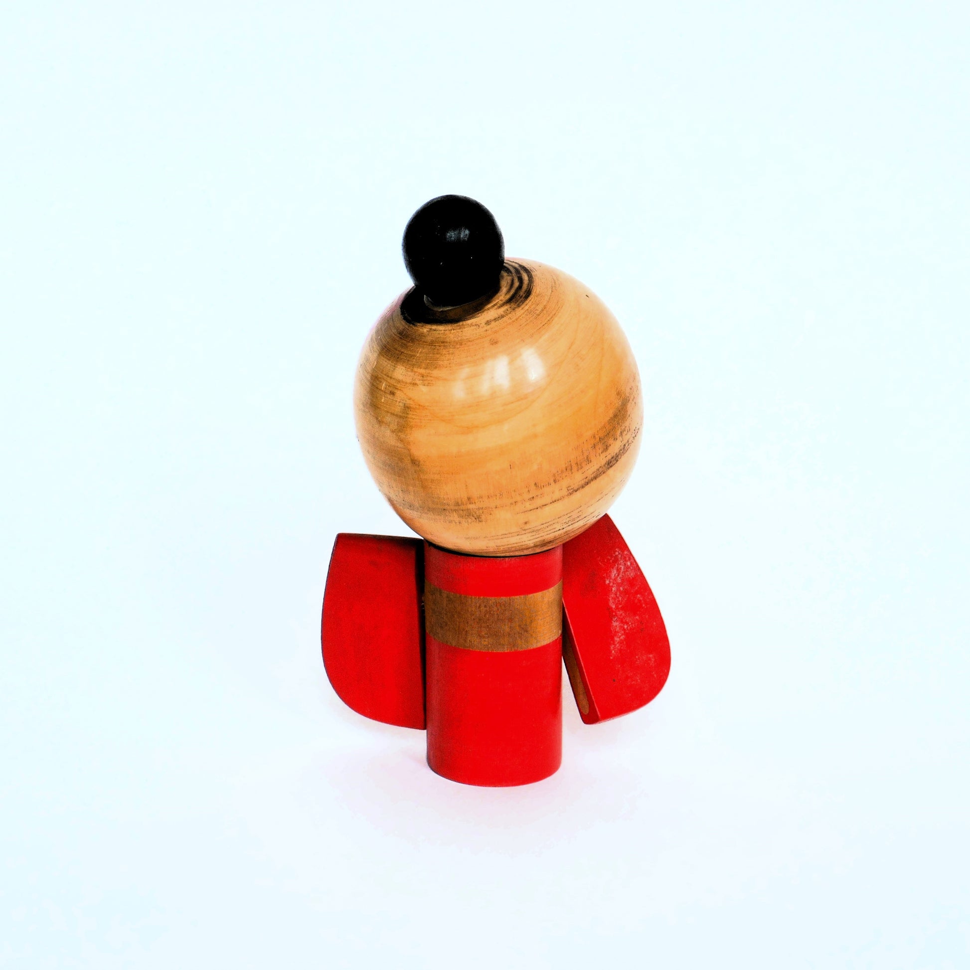 Vue arrière de la kokeshi, montrant la texture du bois et le chignon laqué noir.