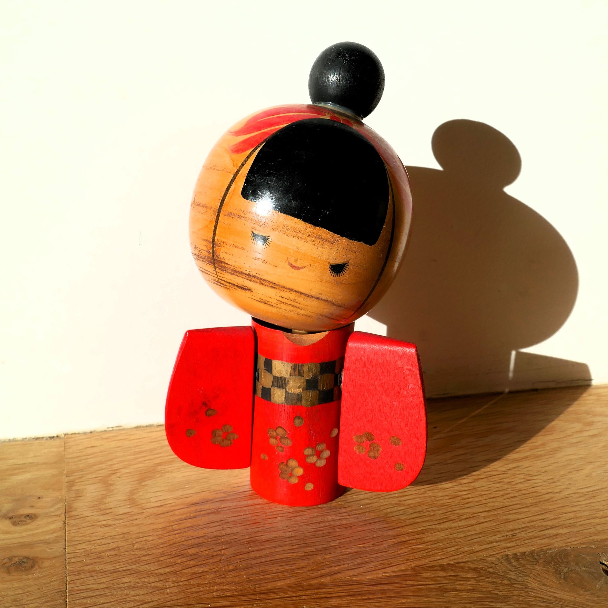 Kokeshi de collection éclairée en lumière naturelle, kimono rouge et expression paisible.