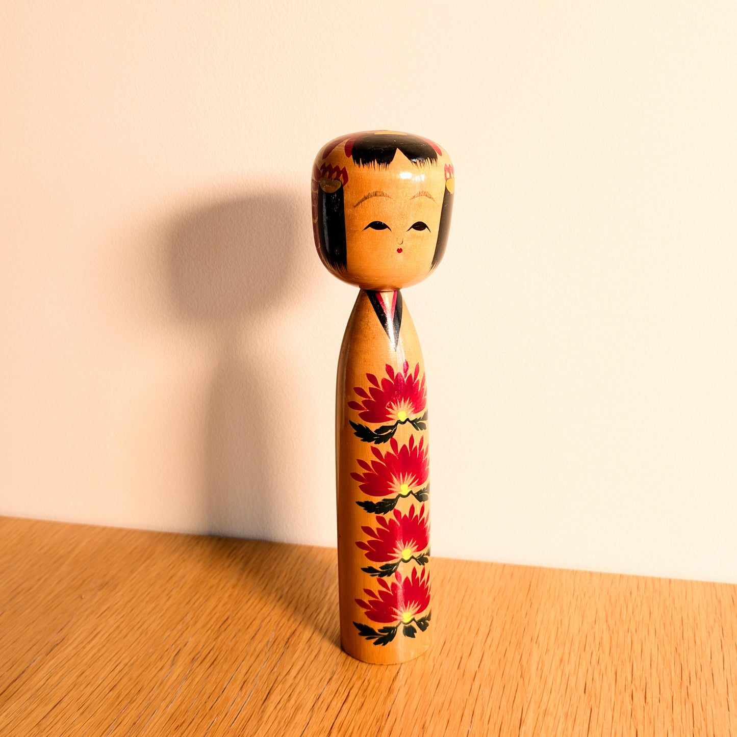 Kokeshi shingata japonaise signée Ryosaku avec motifs kasane giku rouges, visage souriant et belle patine du bois.