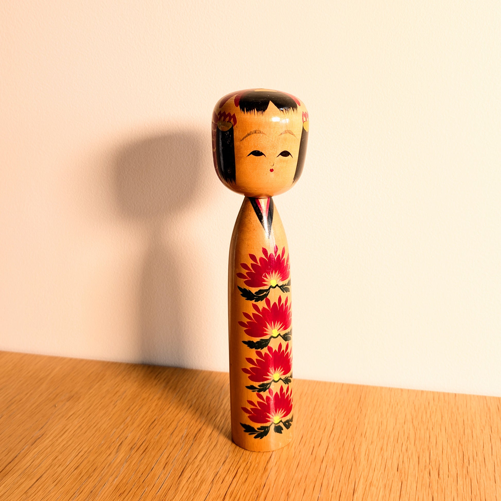 Kokeshi shingata japonaise signée Ryosaku avec motifs kasane giku rouges, visage souriant et belle patine du bois.