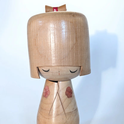 Gros plan du visage sculpté de la kokeshi sōsaku Ueda Izumi, yeux fermés délicats.