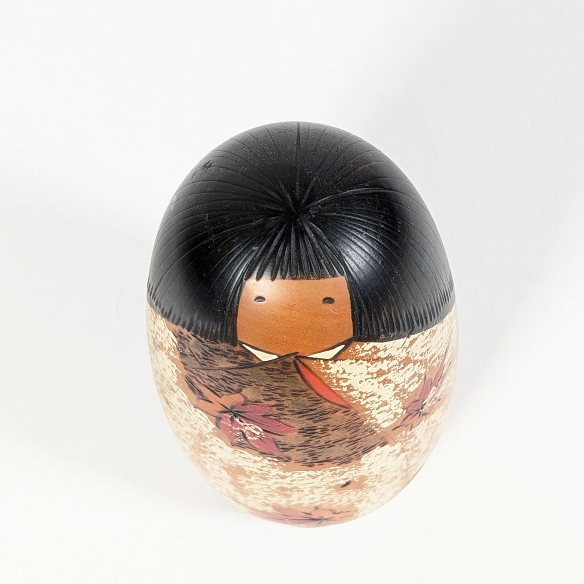 Vue en plongée de la kokeshi Sōsaku Shôzan : chevelure noire finement gravée, petit visage et kimono aux motifs momiji.