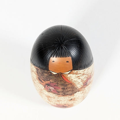 Vue en plongée de la kokeshi Sōsaku Shôzan : chevelure noire finement gravée, petit visage et kimono aux motifs momiji.