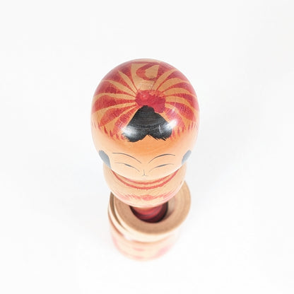 Vue du dessus d’une kokeshi traditionnelle Tōgatta de Nagao Masayoshi, avec décor tegara rouge sur la tête.