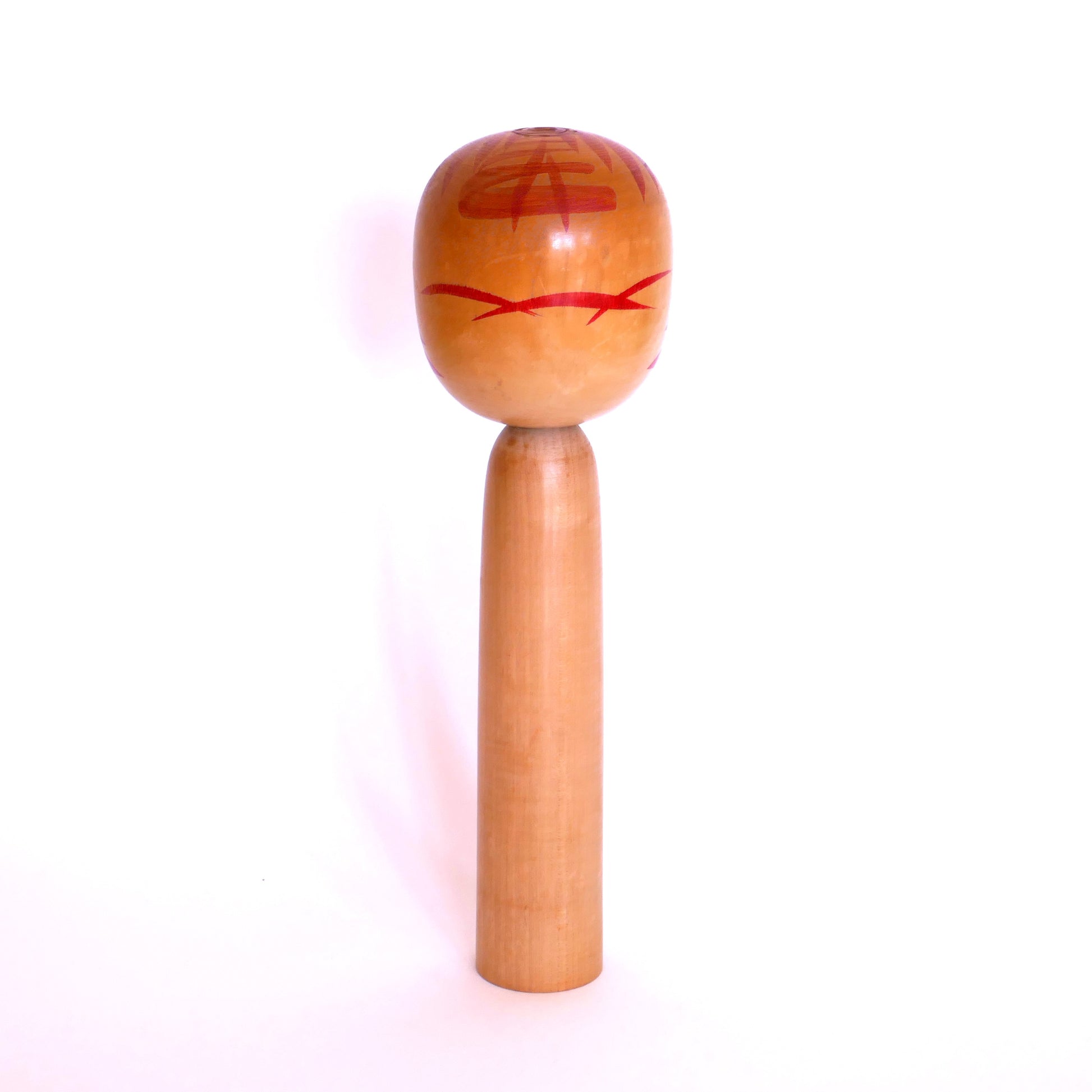 Vue de dos d’une poupée kokeshi Togatta – tête peinte avec motifs solaires rouges typiques de Satō Kesakichi
