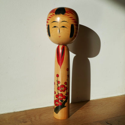Kokeshi Togatta artisanale de Satō Kesakichi vue sous lumère naturelle – poupée japonaise en bois avec fleurs de prunier rouges