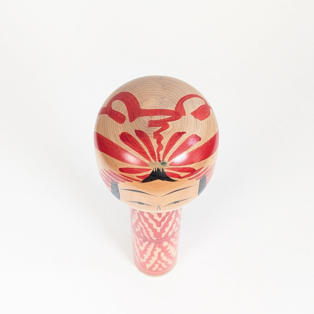 Vue du dessus d’une kokeshi Togatta montrant le motif tegara rouge et noir peint sur la tête en bois tourné