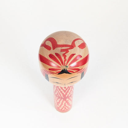 Vue du dessus d’une kokeshi Togatta montrant le motif tegara rouge et noir peint sur la tête en bois tourné