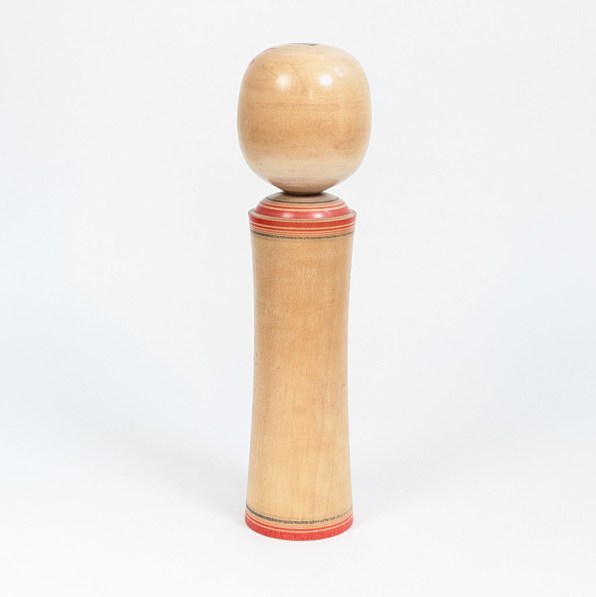 Vue arrière d’une kokeshi traditionnelle Naruko montrant le bois naturel tourné et les lignes rouges peintes à la base et au col.