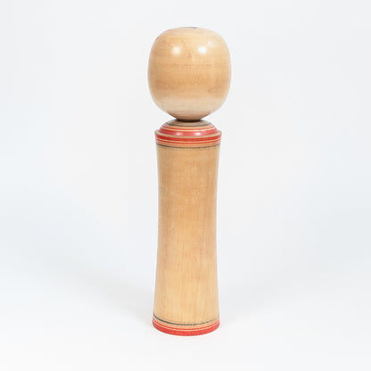 Vue arrière d’une kokeshi traditionnelle Naruko montrant le bois naturel tourné et les lignes rouges peintes à la base et au col.