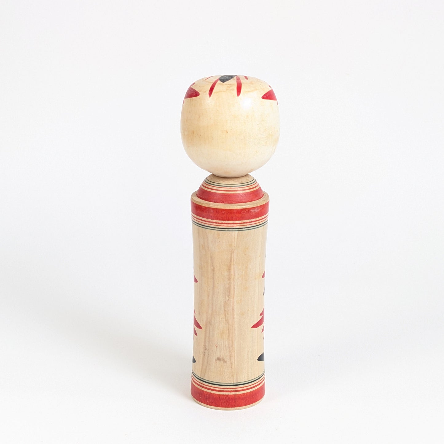 Vue arrière d’une kokeshi traditionnelle de Naruko montrant le bois naturel, les bandes peintes rouges et la forme cylindrique typique.