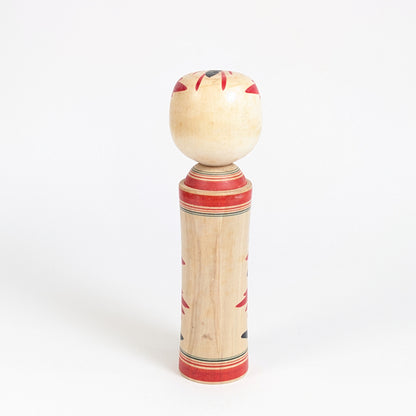 Vue arrière d’une kokeshi traditionnelle de Naruko montrant le bois naturel, les bandes peintes rouges et la forme cylindrique typique.