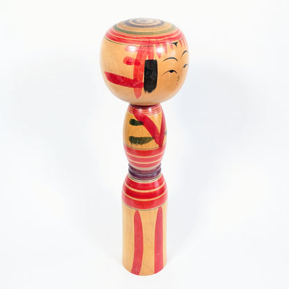Kokeshi traditionnelle Yajirō signée Niiyama Hisashirō, vue de profil avec frange rouge, mèches noires et motifs peints à la main