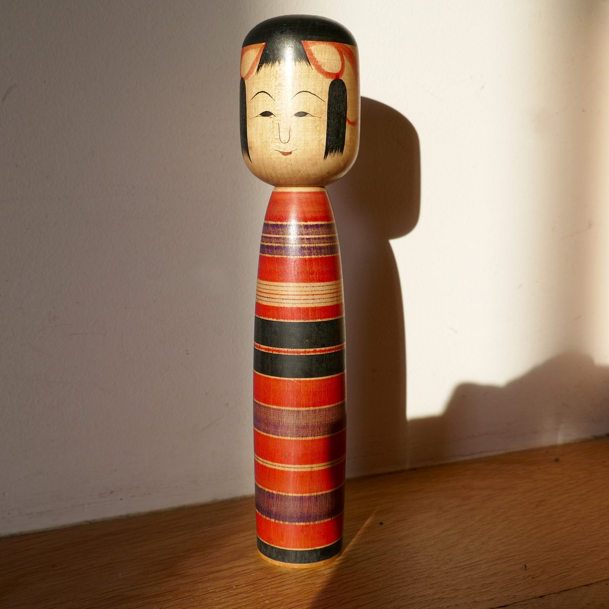 Kokeshi japonaise ancienne Tsuchiyu rouge et noir photographiée en lumière naturelle