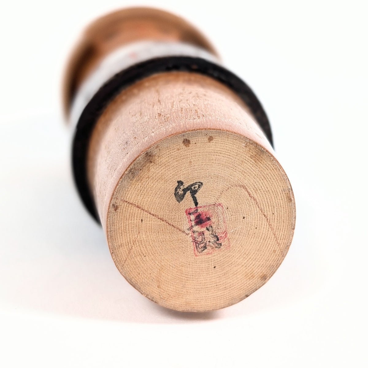 Dessous de la base en bois d'une kokeshi vintage attribuée à l'atelier Usaburo, présentant la signature Usaburo calligraphiée à l'encre noire et un cachet rouge partiellement effacé.