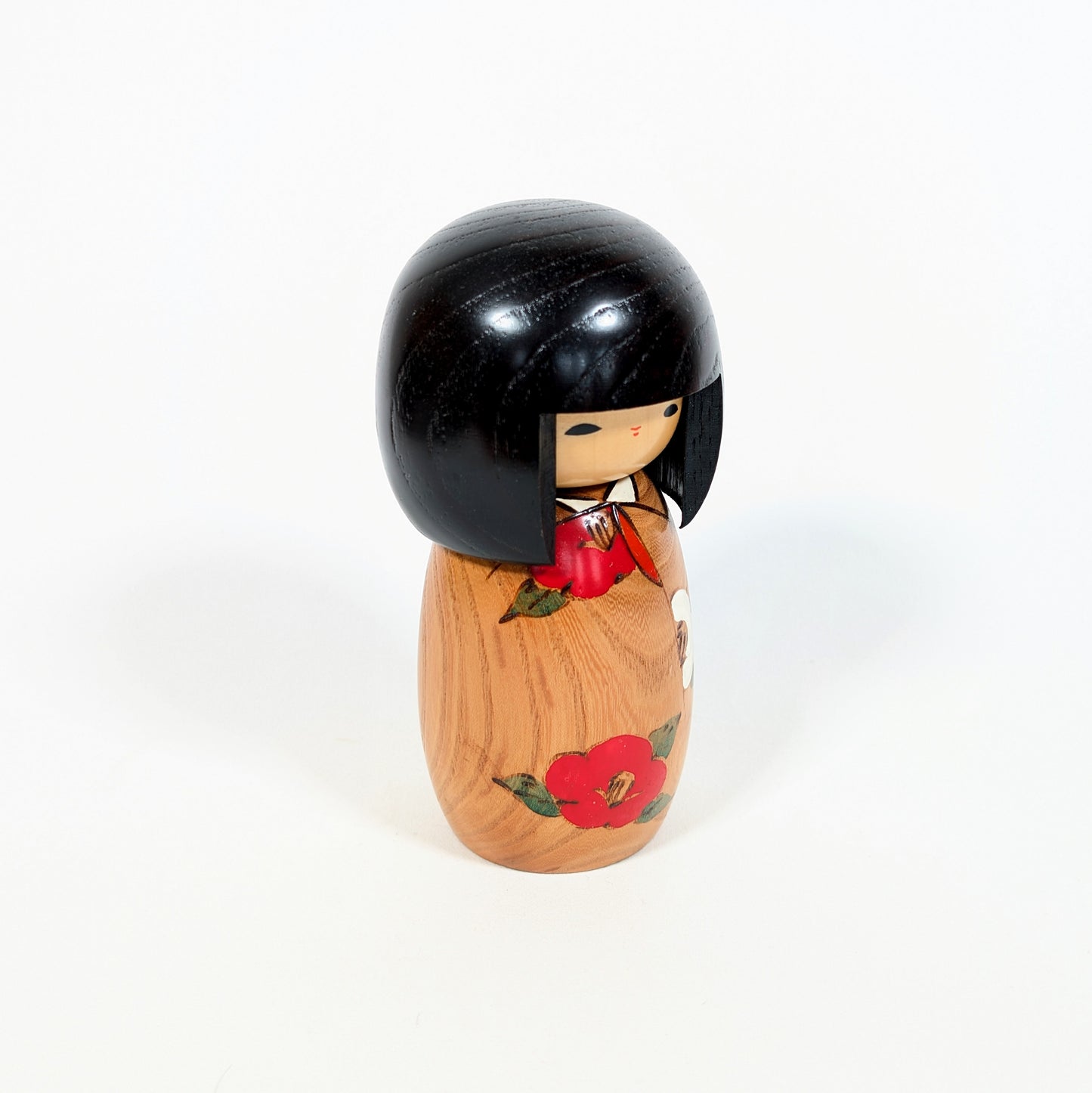Profil d’une poupée japonaise kokeshi Usaburo Haru no uta avec bois veiné, cheveux noirs laqués et fleur de camélia rouge