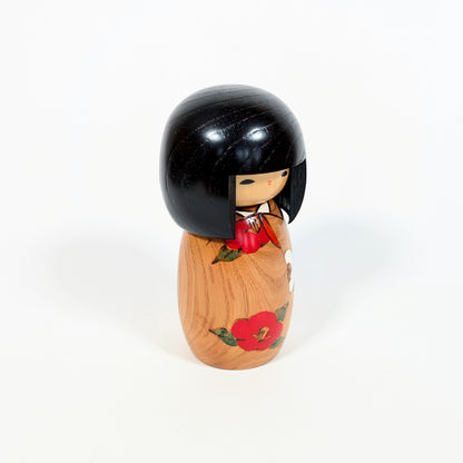 Profil d’une poupée japonaise kokeshi Usaburo Haru no uta avec bois veiné, cheveux noirs laqués et fleur de camélia rouge