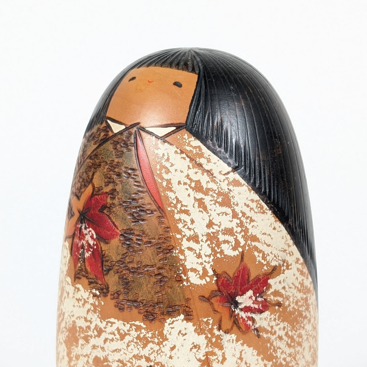 Gros plan de la kokeshi japonaise vintage Usaburo Shôzan : visage souriant, cheveux noirs sculptés et kimono orné de feuilles d’érable.