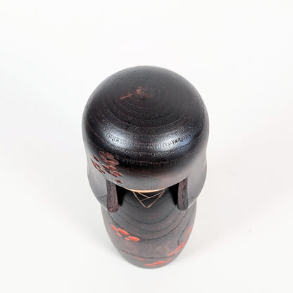 Vue du dessus d’une kokeshi Usaburo avec coiffure okappa en bois foncé