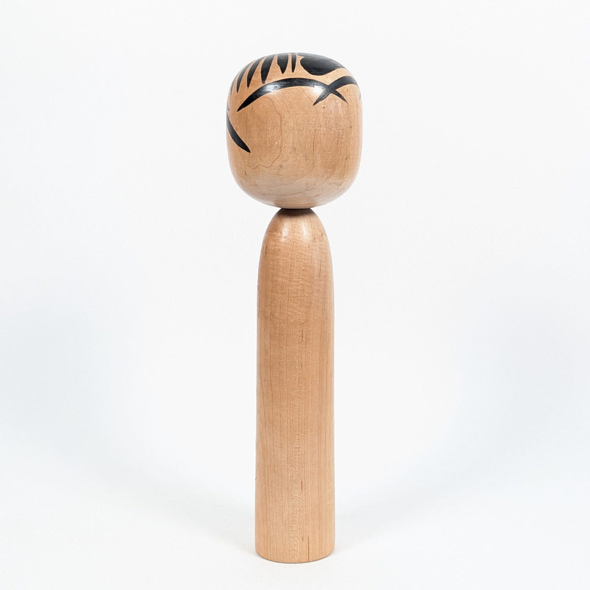 Vue arrière d'une kokeshi vintage japonaise, montrant son corps en bois tourné et les motifs noirs de sa chevelure.