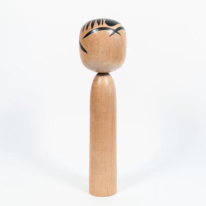 Vue arrière d'une kokeshi vintage japonaise, montrant son corps en bois tourné et les motifs noirs de sa chevelure.