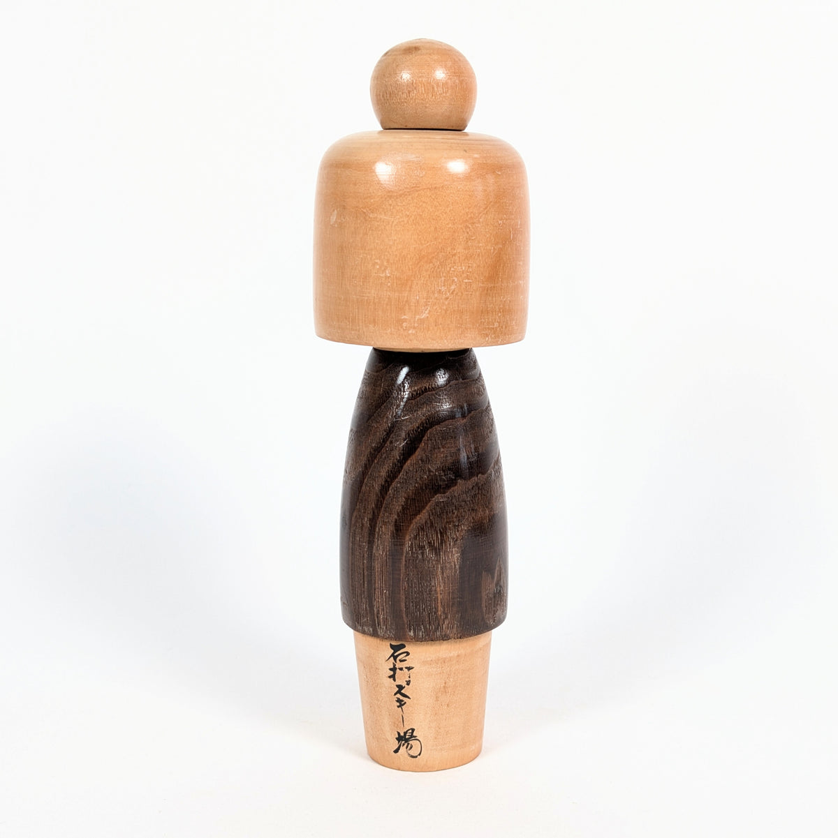 Vue arrière d'une kokeshi vintage japonaise Usaburo de l'époque Shōwa, montrant le veinage du bois brun foncé, la coiffure sculptée et une inscription japonaise.