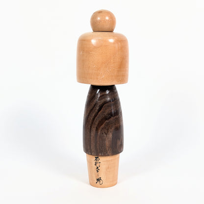 Vue arrière d'une kokeshi vintage japonaise Usaburo de l'époque Shōwa, montrant le veinage du bois brun foncé, la coiffure sculptée et une inscription japonaise.