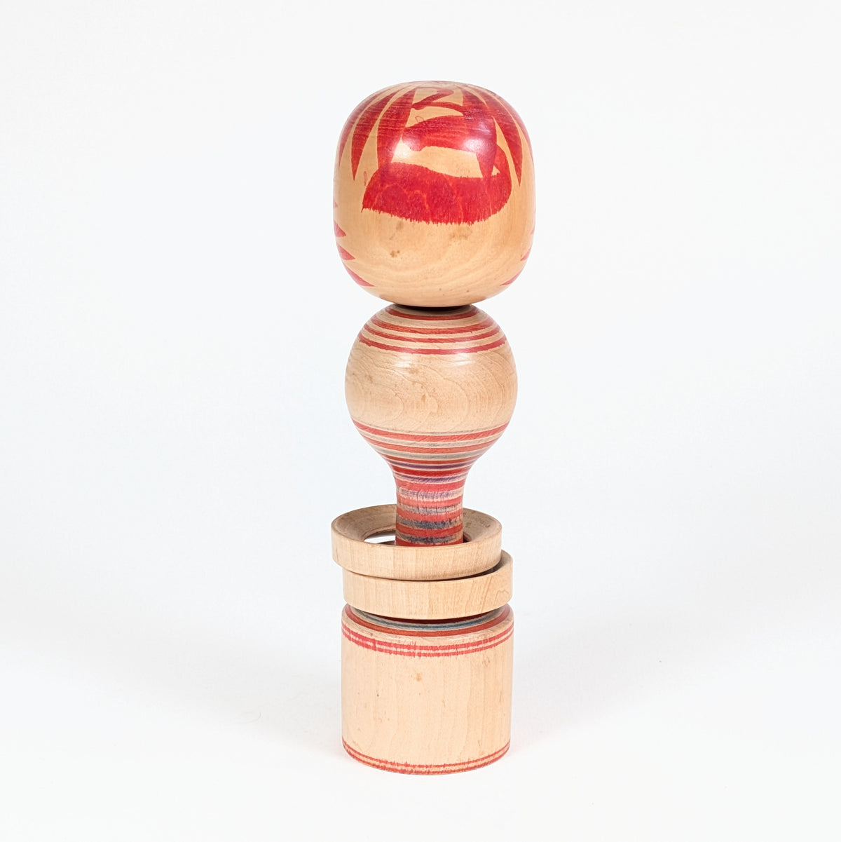 Vue arrière d’une kokeshi vintage Tōgatta, avec tegara rouge et décor circulaire rokuro-moyō peint au tour.