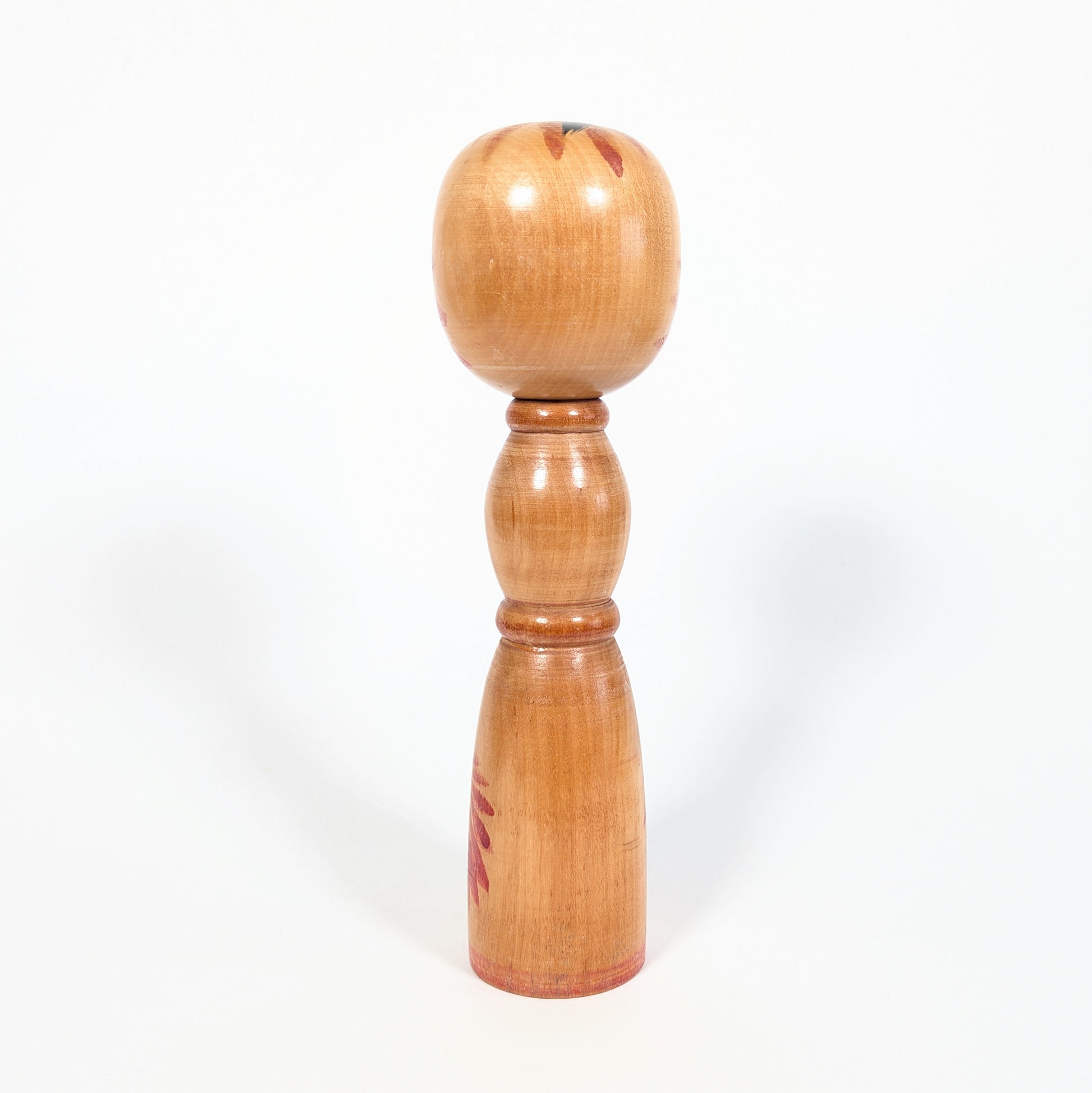 Dos d’une kokeshi vintage japonaise Yajirō, bois naturel verni, forme shingata élancée et décor floral rouge partiel