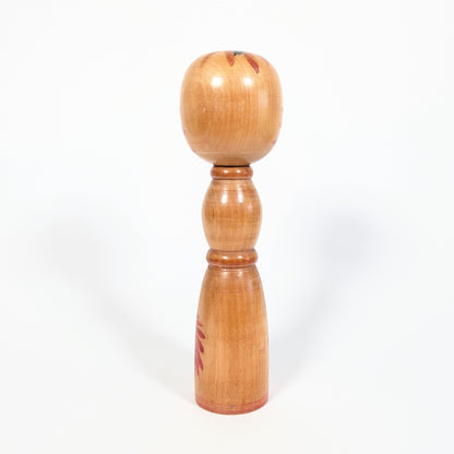 Dos d’une kokeshi vintage japonaise Yajirō, bois naturel verni, forme shingata élancée et décor floral rouge partiel