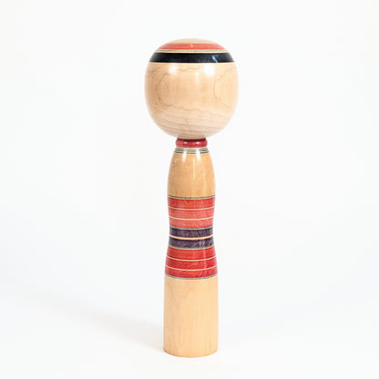 Dos d’une kokeshi vintage Yajiro avec bandes circulaires rokuro-moyo rouges et violettes sur bois naturel