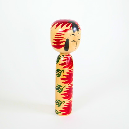 une poupée kokeshi en bois de style hijiori yamagata signée Kobayashi Shozo vue de trois quarts rouge et verte