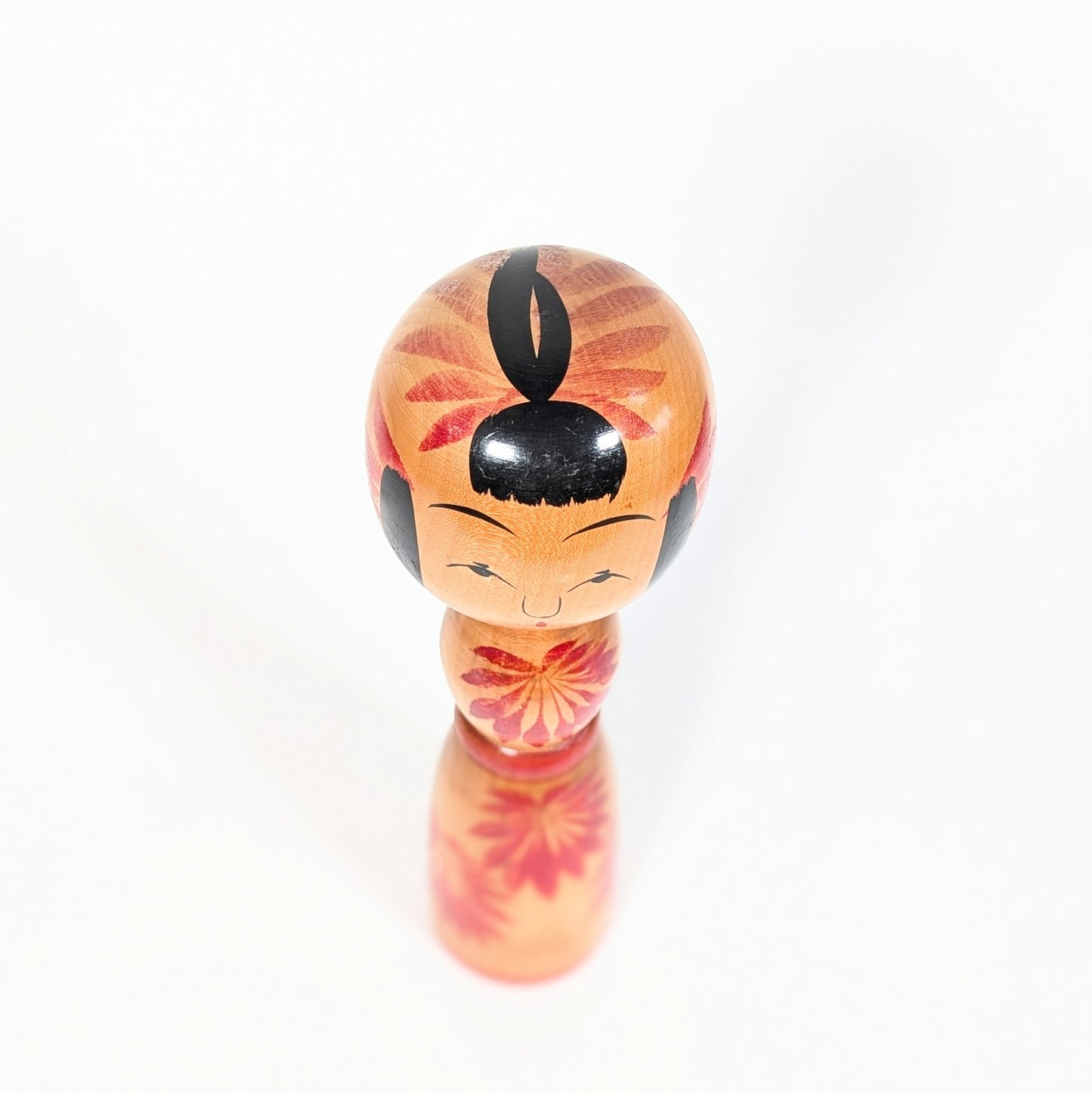 Vue de dessus d’une kokeshi Yajirō shingata, coiffure noire stylisée et décor floral rouge autour de la tête