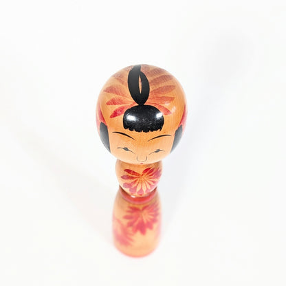 Vue de dessus d’une kokeshi Yajirō shingata, coiffure noire stylisée et décor floral rouge autour de la tête