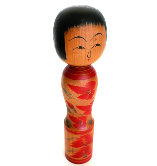 Vue en plongée d’une kokeshi artisanale montrant la coiffure peinte et les épaules.