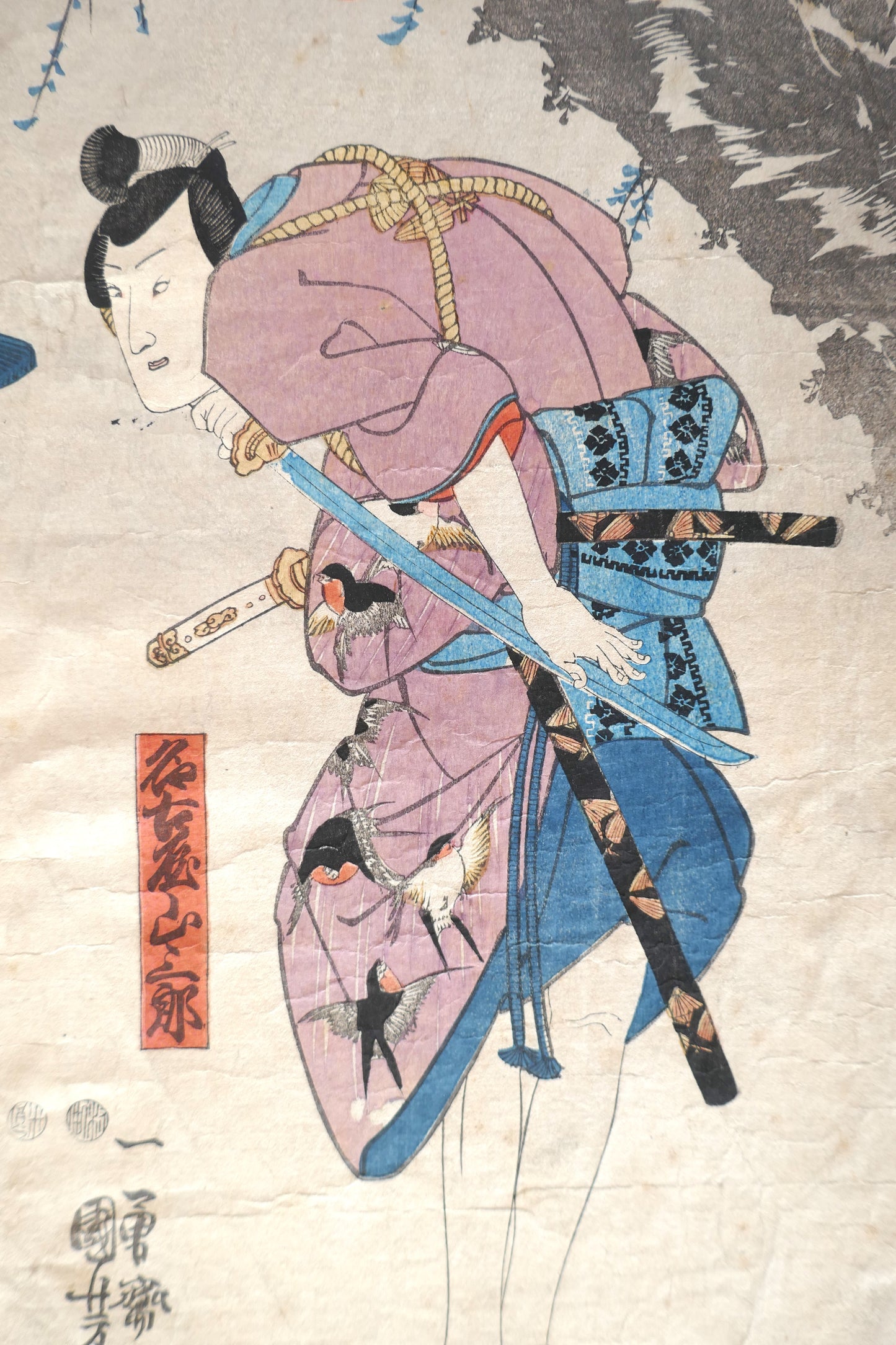 Gros plan sur le personnage principal de l’estampe : acteur de kabuki en kimono violet orné d’hirondelles.