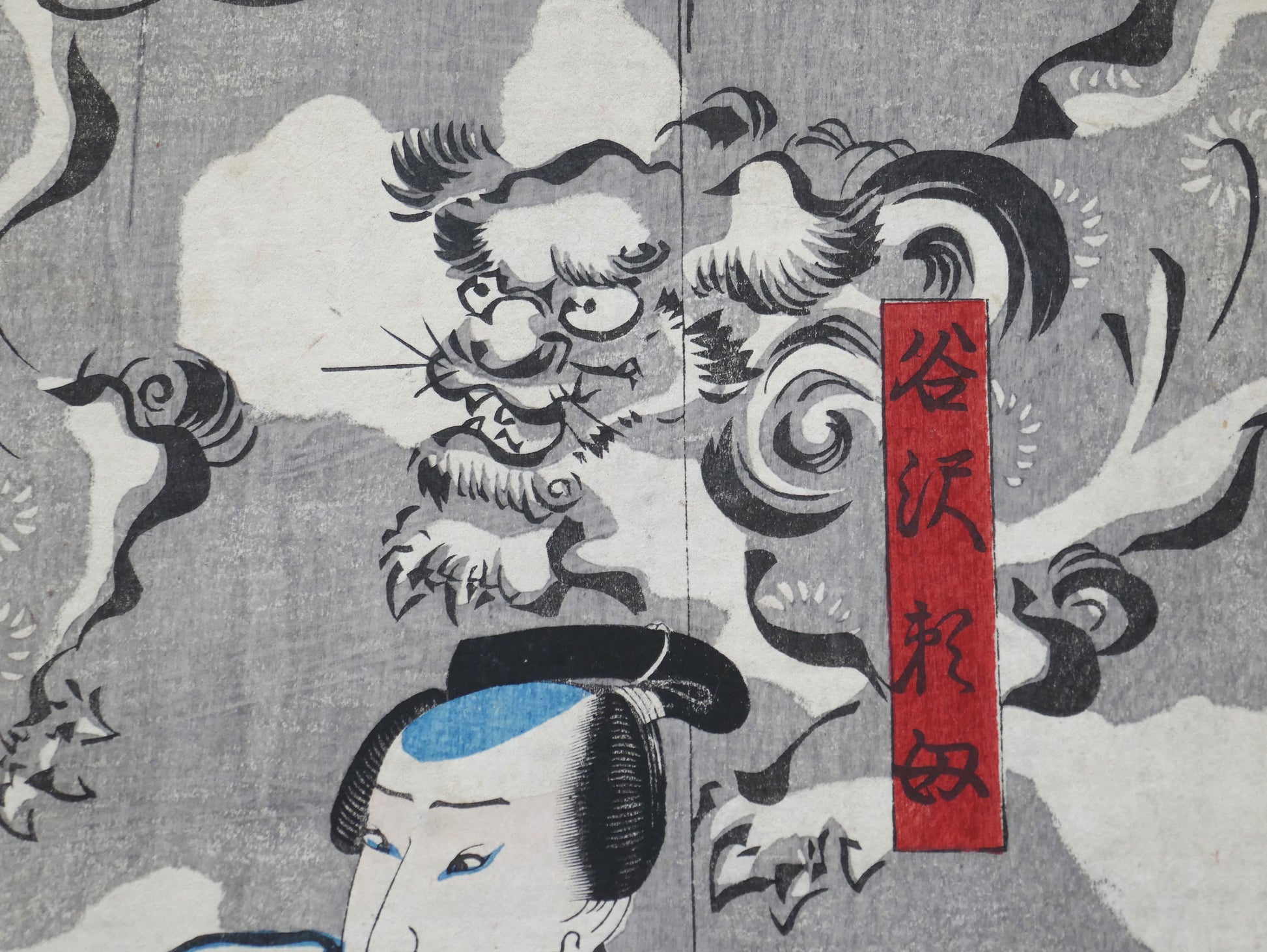 Cartouche rouge portant le nom Tanizawa Tanomo sur fond de nuées et shishi, détail de l’estampe kabuki de Kuniyoshi (Edo, 1849).