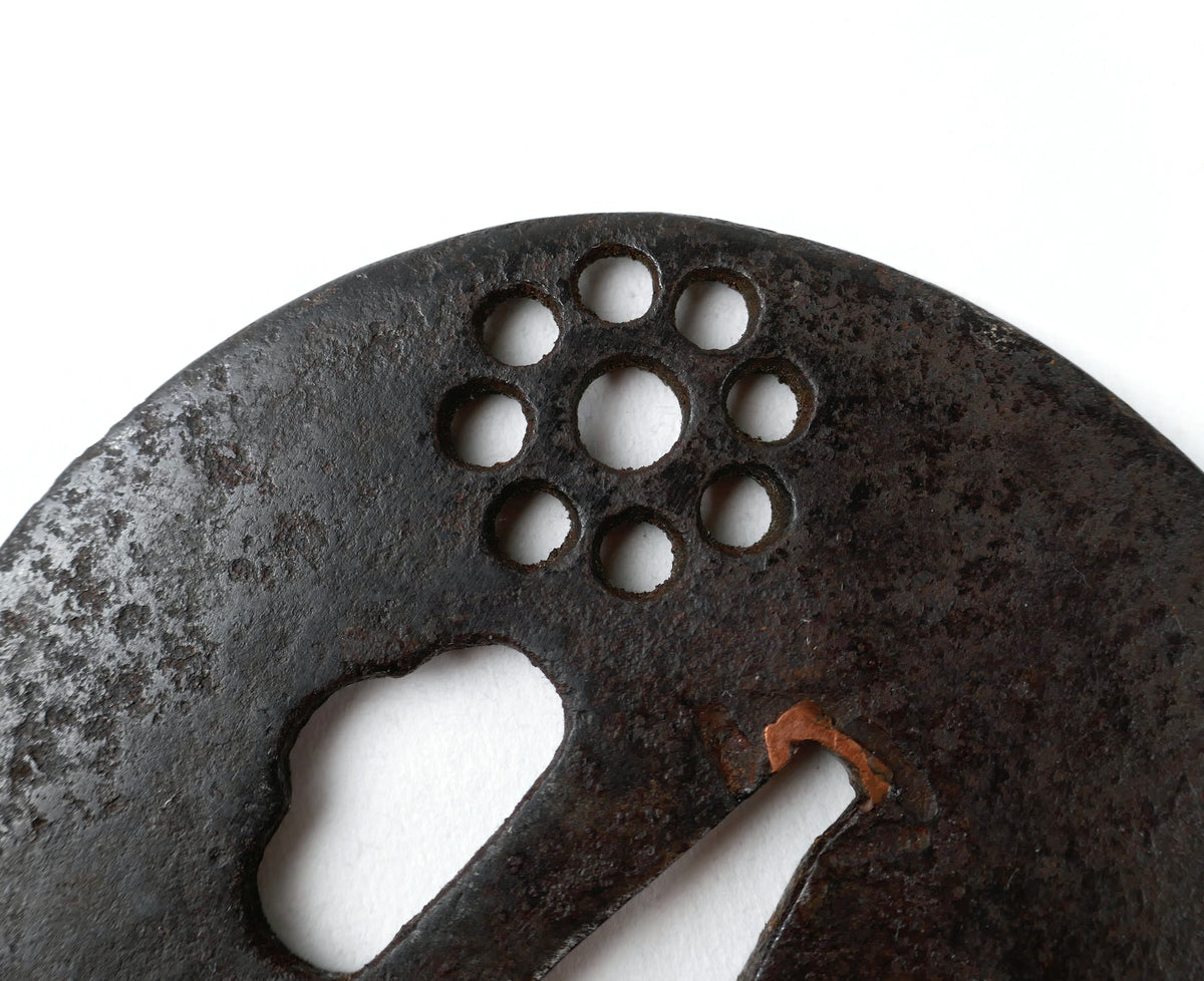 Gros plan du Kuyō-mon, motif japonais des Neuf Astres ajouré en sukashi sur une ancienne tsuba en fer.