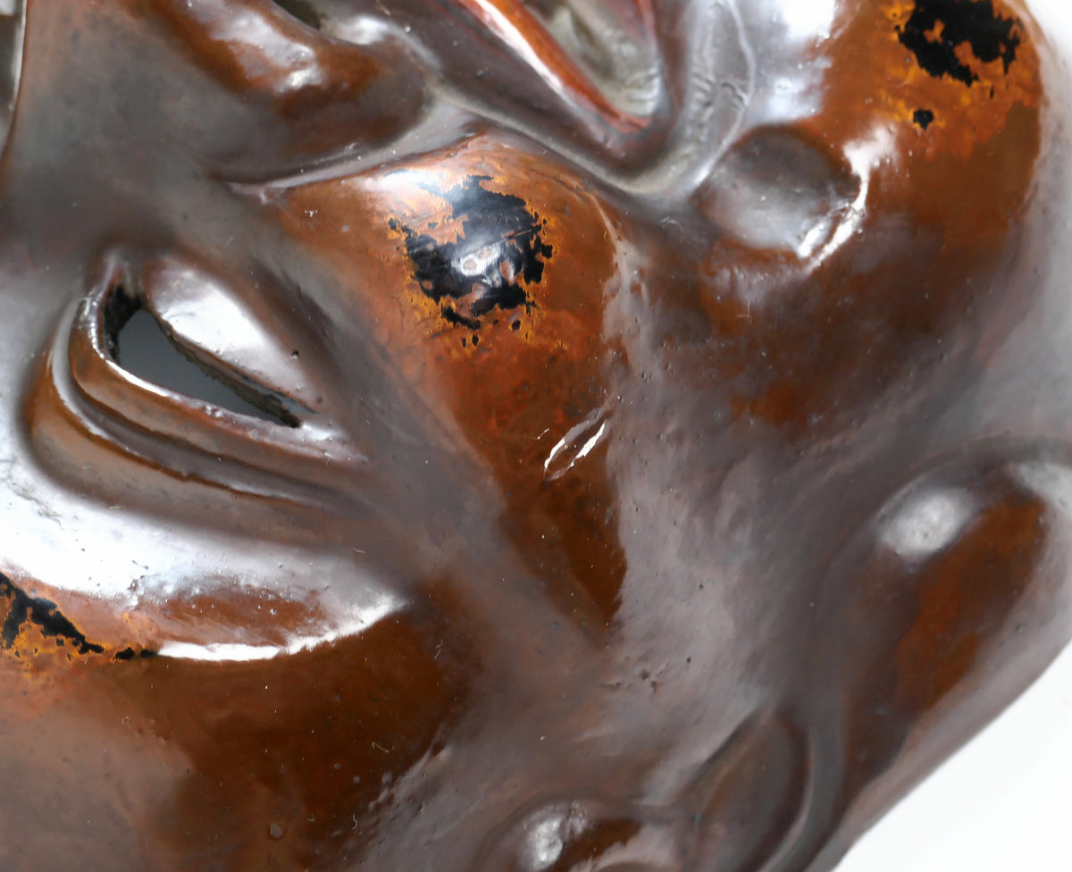 Gros plan sur la joue d’un masque Daikoku montrant la laque brun-rouge polie et la couche noire sous-jacente, effet de type Negoro.