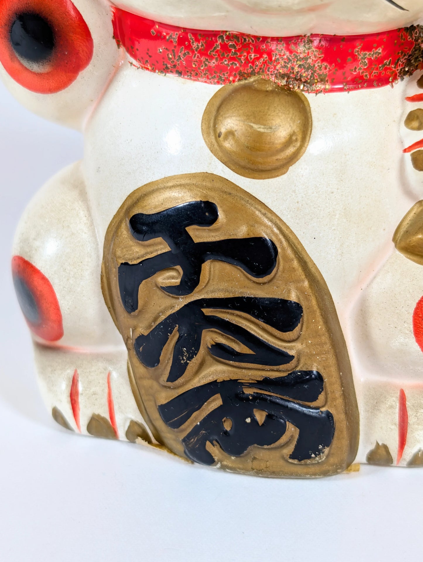 Détail de la plaque dorée du maneki-neko montrant les kanji 千万両 symbolisant une grande richesse, artisanat japonais vintage.