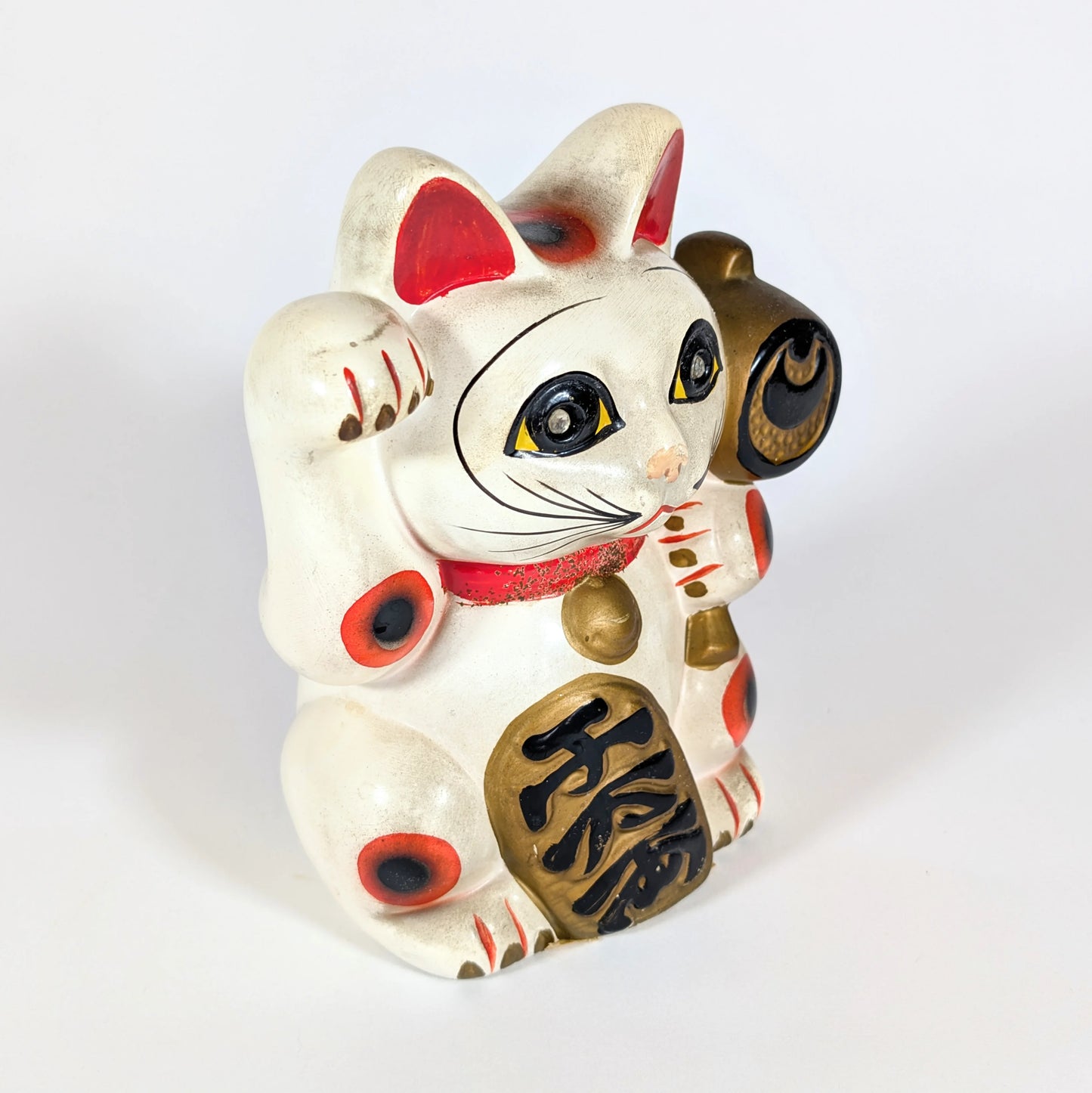 Profil droit d’un maneki-neko ancien en céramique, chat japonais porte-bonheur tenant un marteau uchide no kozuchi.