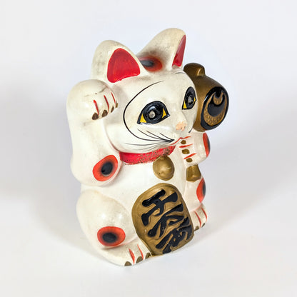 Profil droit d’un maneki-neko ancien en céramique, chat japonais porte-bonheur tenant un marteau uchide no kozuchi.