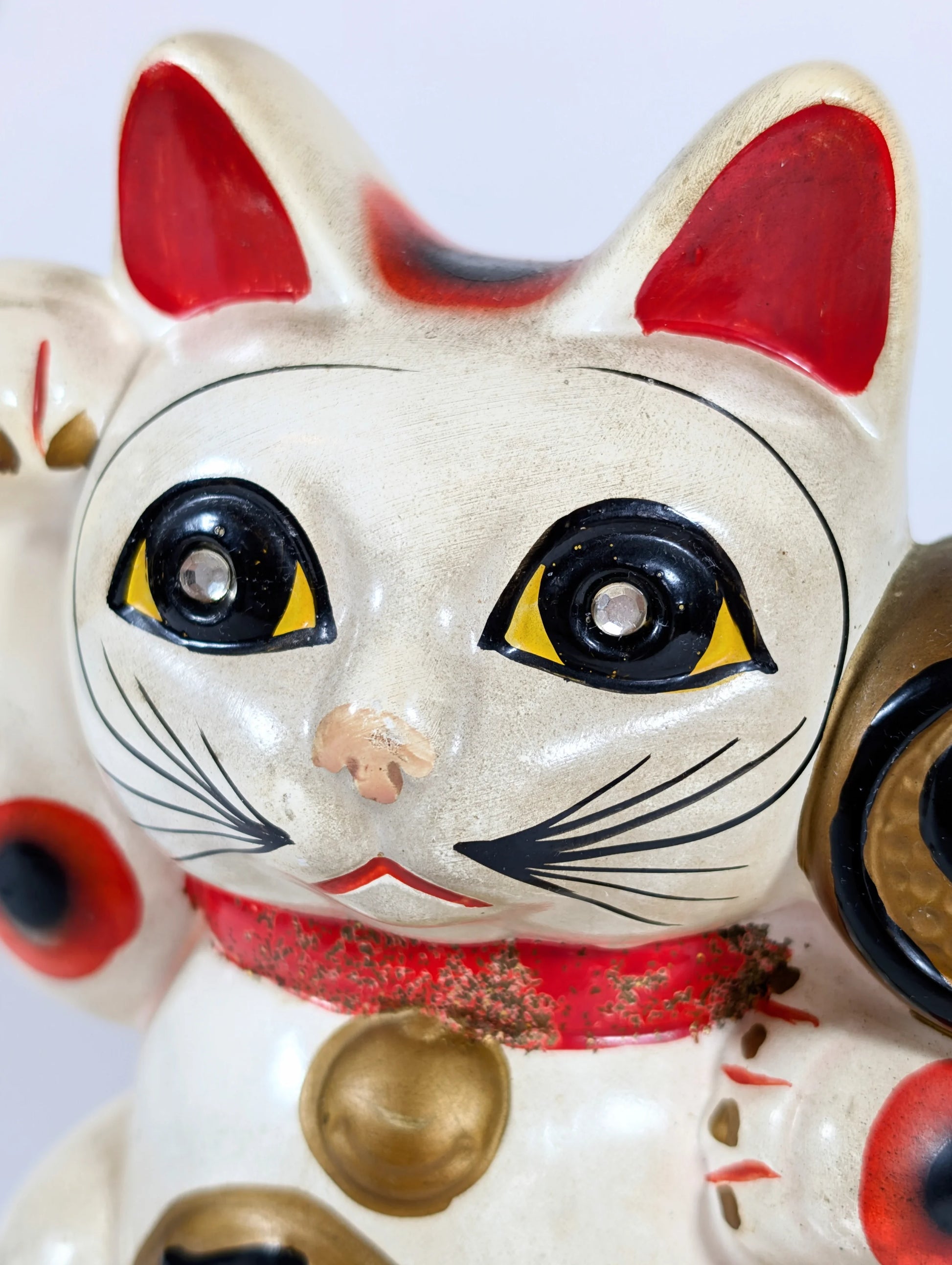 Gros plan du visage d’un maneki-neko vintage, chat japonais porte-bonheur aux yeux ornés de strass.