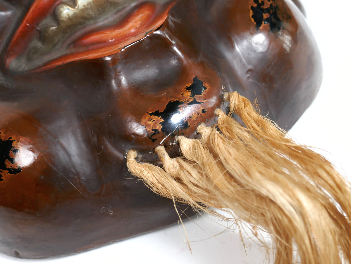 Détail du menton d’un masque japonais Daikoku avec barbe en fibres végétales de type chanvre et finition en laque rouge sur noir.