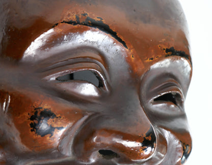 Gros plan des yeux d’un masque de Daikoku en laque japonaise rouge-brun et noire, montrant le travail de polissage de la surface.